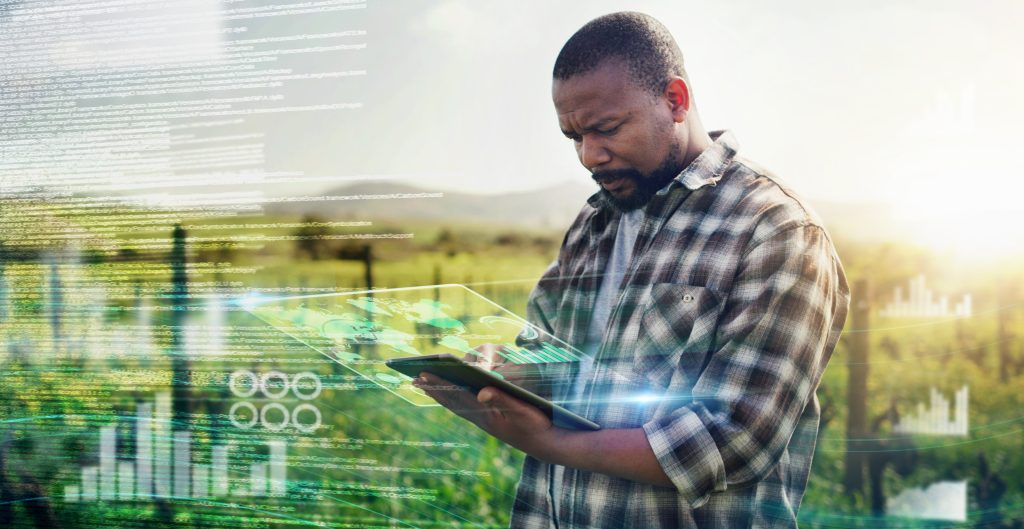 Man in a field with a tablet and the image of data swirling in the air.